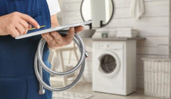 A plumber uses a tablet computer while holding a hose in a neutral bathroom.
