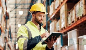 Man in factory wearing hard hat looking up details on tablet