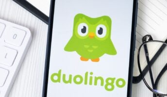 Duolingo logo on phone on desk with glasses and keyboard